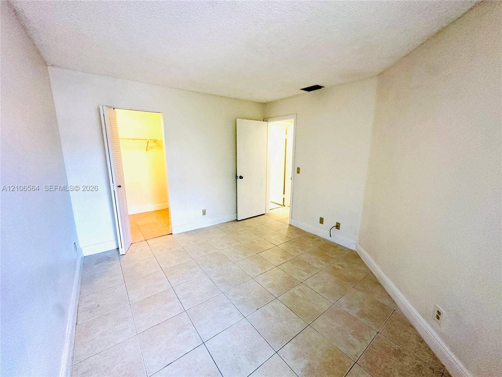 Neutral-toned room featuring large-format ceramic tile flooring, a walk-in closet with integrated shelving, and solid-core interior doors