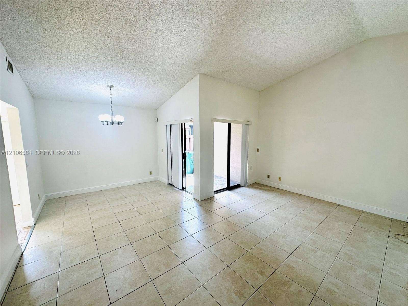Vaulted ceilings, large-format tile flooring, dual sliding glass doors, and a multi-arm pendant light fixture