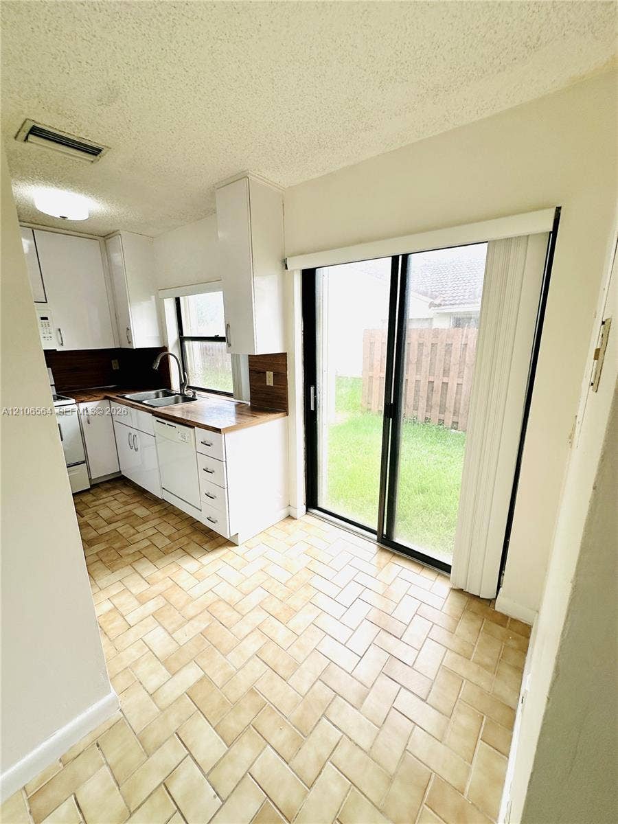 Kitchen featuring white cabinetry, wood-finish countertops, stainless steel dual-basin sink, herringbone-patterned tile flooring, and sliding glass doors