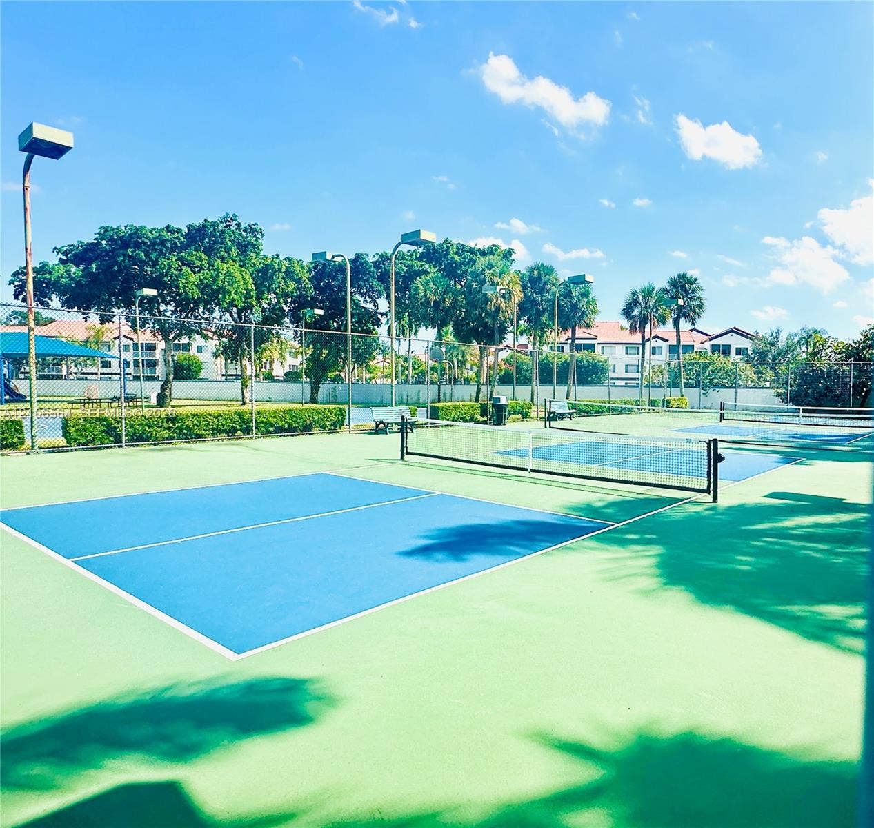 Multi-court pickleball facility featuring high-visibility blue and green court surfaces, chain-link perimeter fencing, pole-mounted lighting, and integrated seating areas