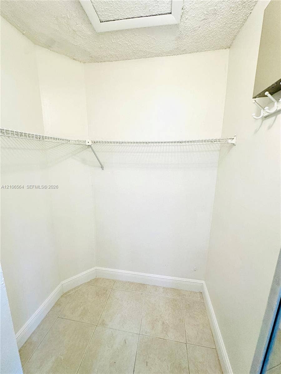 Storage space featuring white walls, light-toned tile flooring, built-in wire shelving, and a wall-mounted hook rack