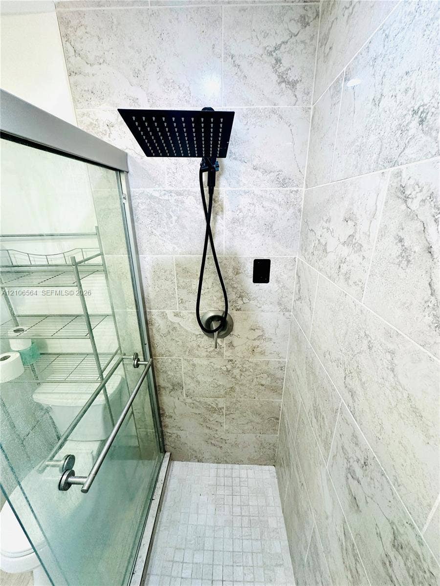 Walk-in shower enclosure featuring large-format stone-patterned wall tile, square rainfall showerhead, integrated handheld sprayer, and mosaic tile flooring