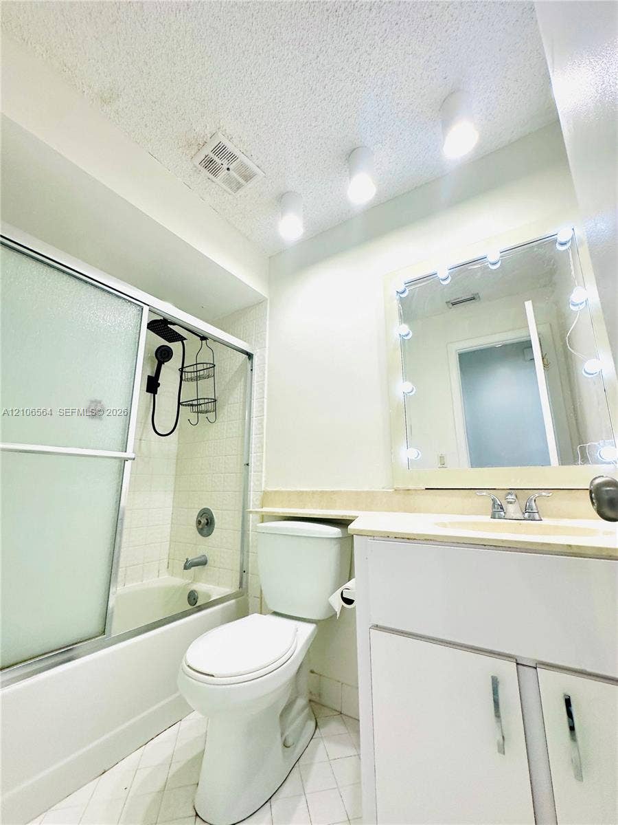 Bathroom featuring a white vanity cabinet, surface-mount vanity mirror with integrated lighting, shower-tub combination with sliding glass doors, and tile flooring