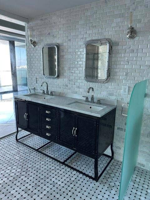 Double vanity featuring a black metal frame, integrated countertop with dual rectangular undermount sinks, two polished-metal port-style wall mirrors, brick-style wall tiling, and dual-toned mosaic floor tile