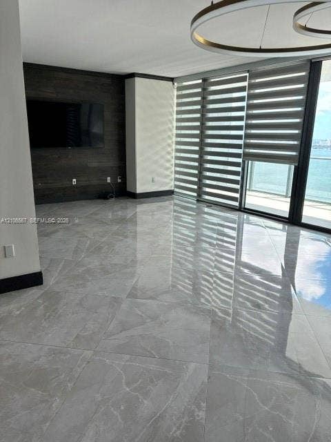 Large-format polished tile flooring, dark wood-tone accent wall, floor-to-ceiling windows with integrated roller shades, and contemporary circular ceiling lighting