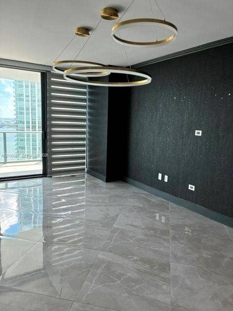 Polished stone-finish flooring, dual-ring LED pendant lighting with metallic finish, textured dark accent wall, and floor-to-ceiling sliding glass door with integrated window treatments