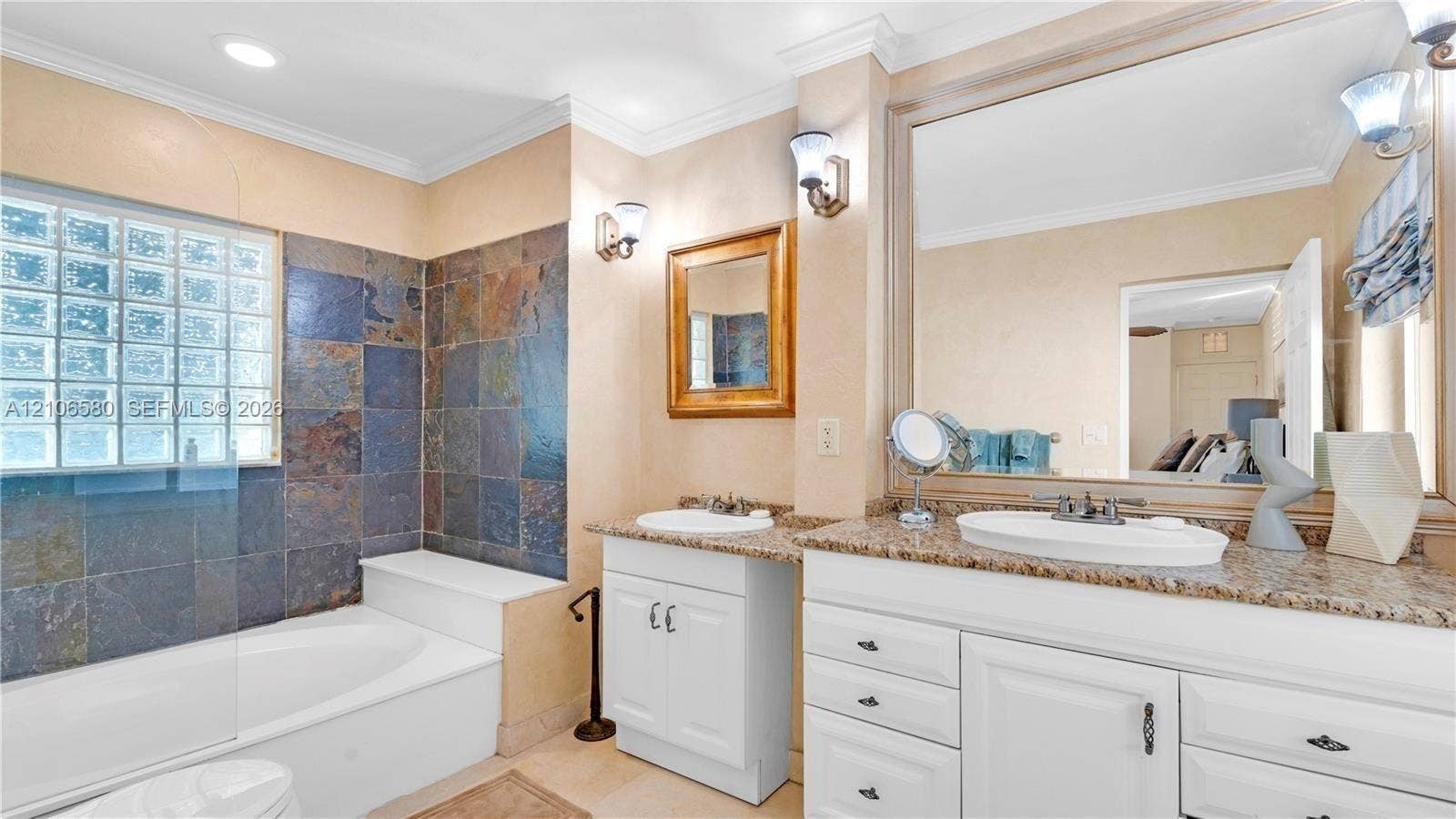 623 NE 17th Way, Fort Lauderdale, Fort Lauderdale, FL 33304 Bathroom featuring dual white vanities with stone countertops, undermount sinks, glass block window, and slate tile surround at the soaking tub