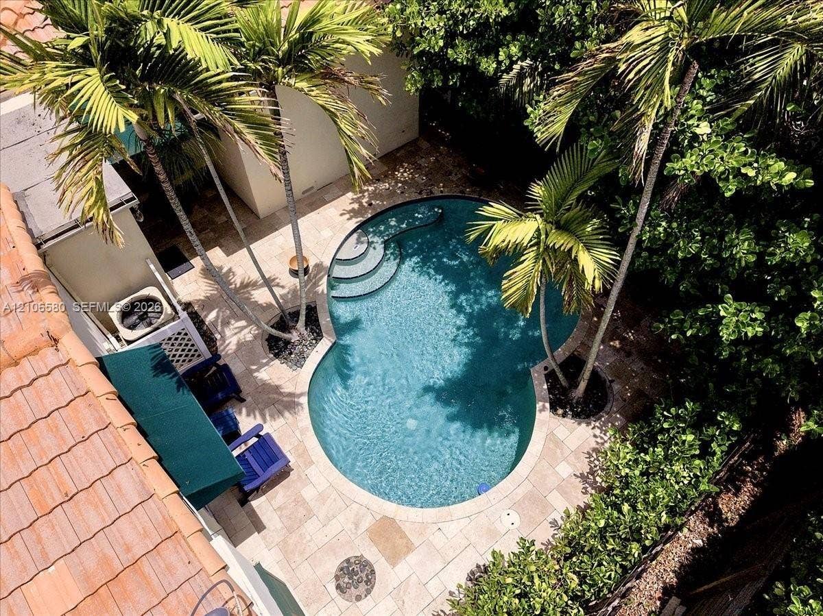 623 NE 17th Way, Fort Lauderdale, Fort Lauderdale, FL 33304 Curved swimming pool with built-in stairs, surrounded by stone-tile patio decking, mature palm trees, and perimeter landscaping