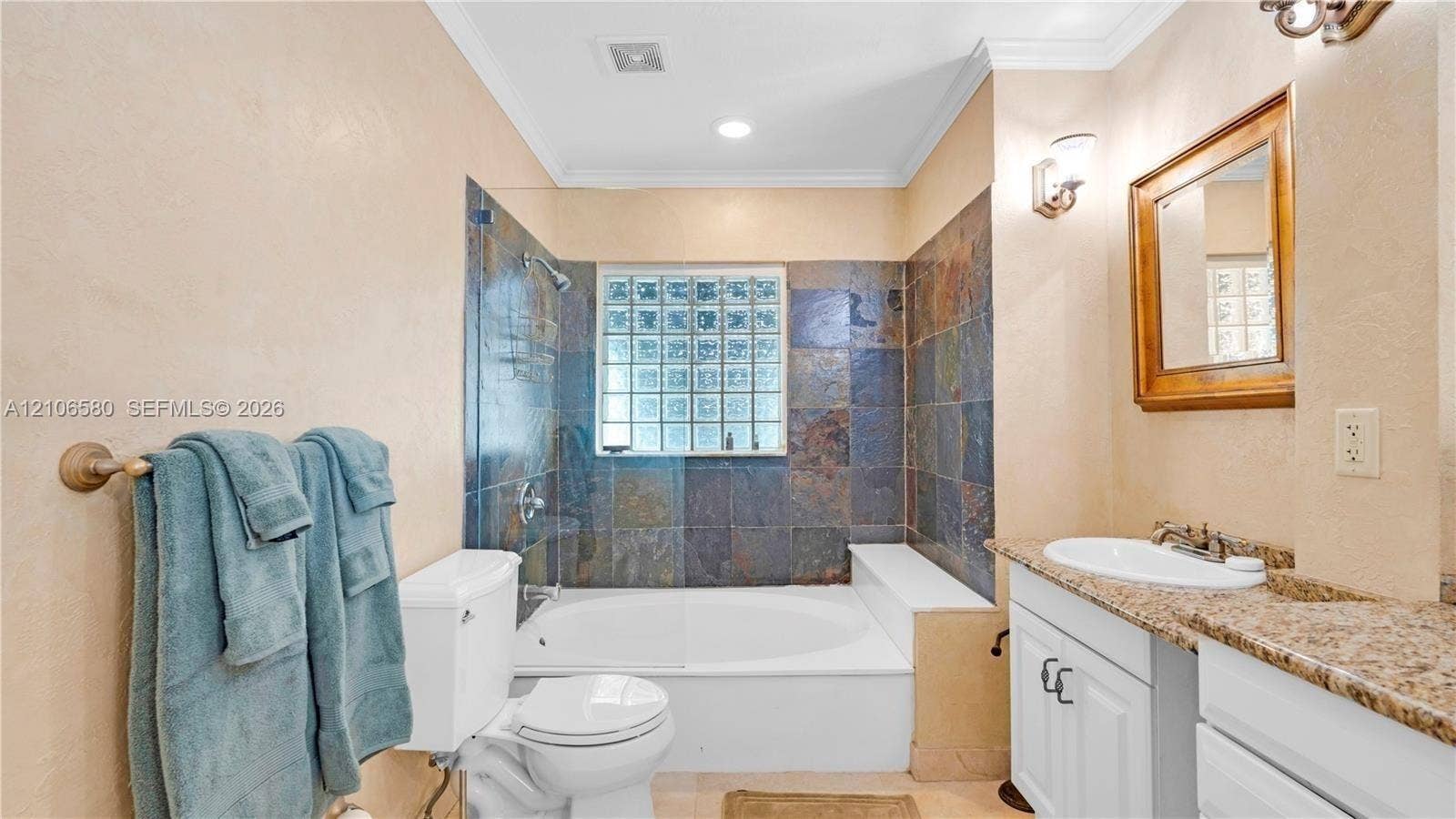 623 NE 17th Way, Fort Lauderdale, Fort Lauderdale, FL 33304 Bathroom featuring a stone-tile tub surround, glass-block window, undermount sink with a stone countertop, white shaker-style vanity cabinetry, and wall-mounted light fixtures