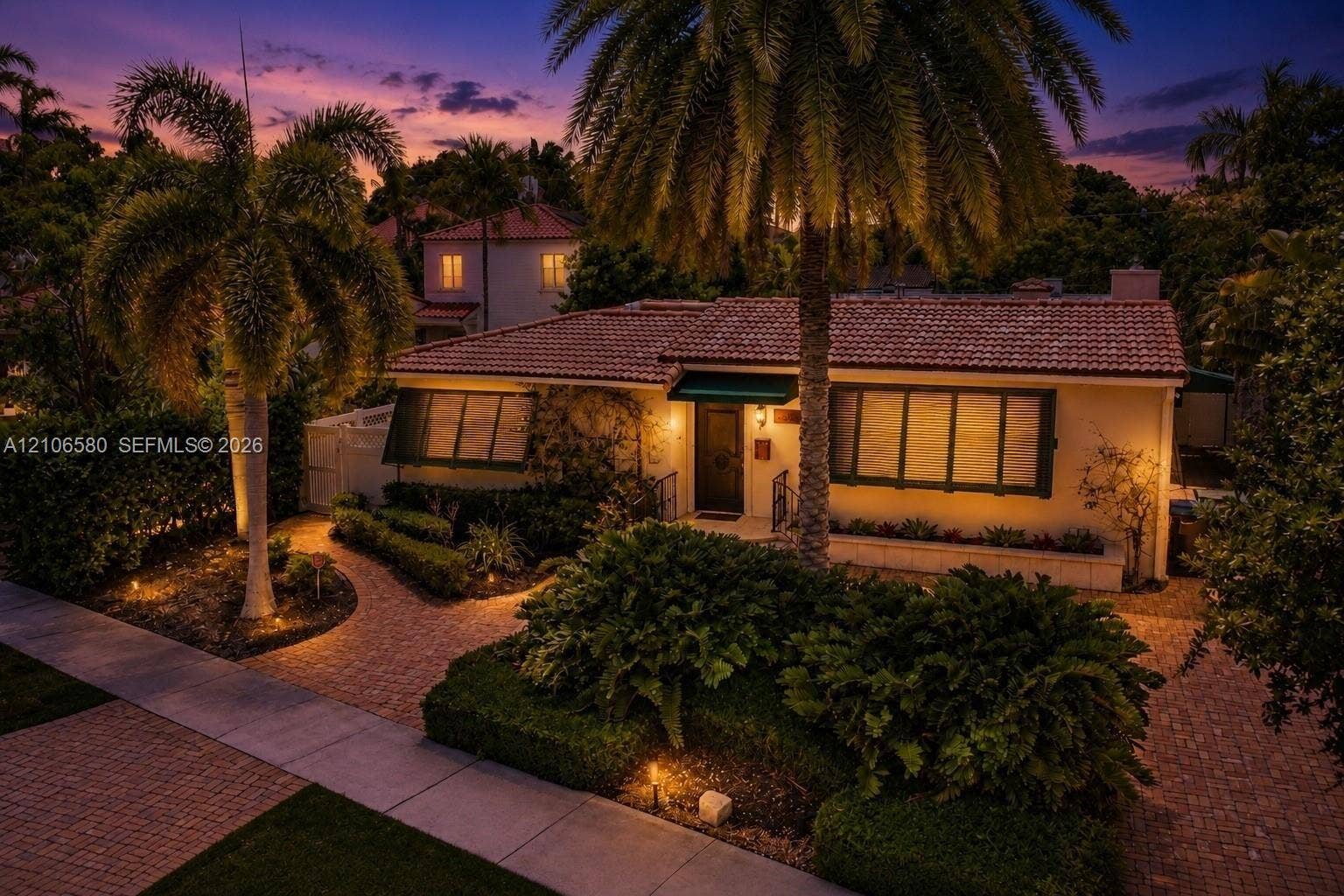 623 NE 17th Way, Fort Lauderdale, Fort Lauderdale, FL 33304 Single-story residence featuring a tile roof, paved walkway, mature palm trees, manicured hedges, and exterior wall-mounted lighting