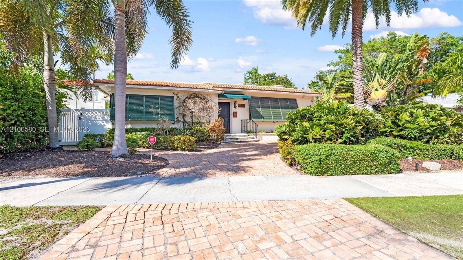 623 NE 17th Way, Fort Lauderdale, Fort Lauderdale, FL 33304 Single-story residence featuring a brick-paved driveway, clay tile roof, metal window awnings, and mature landscaping
