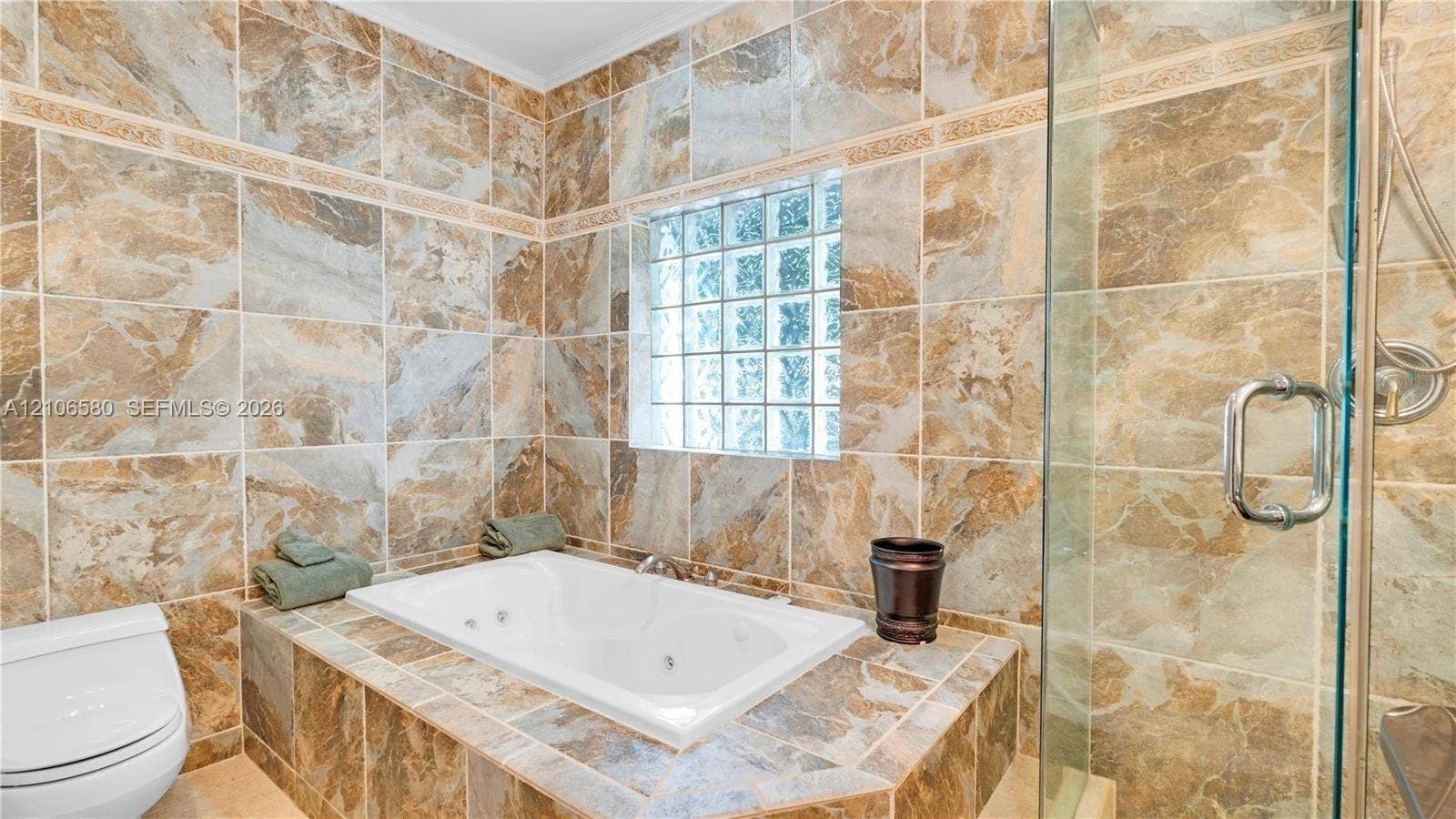 623 NE 17th Way, Fort Lauderdale, Fort Lauderdale, FL 33304 Full-wall patterned tile surround, drop-in jetted soaking tub, glass block window, and glass-enclosed shower with metallic hardware