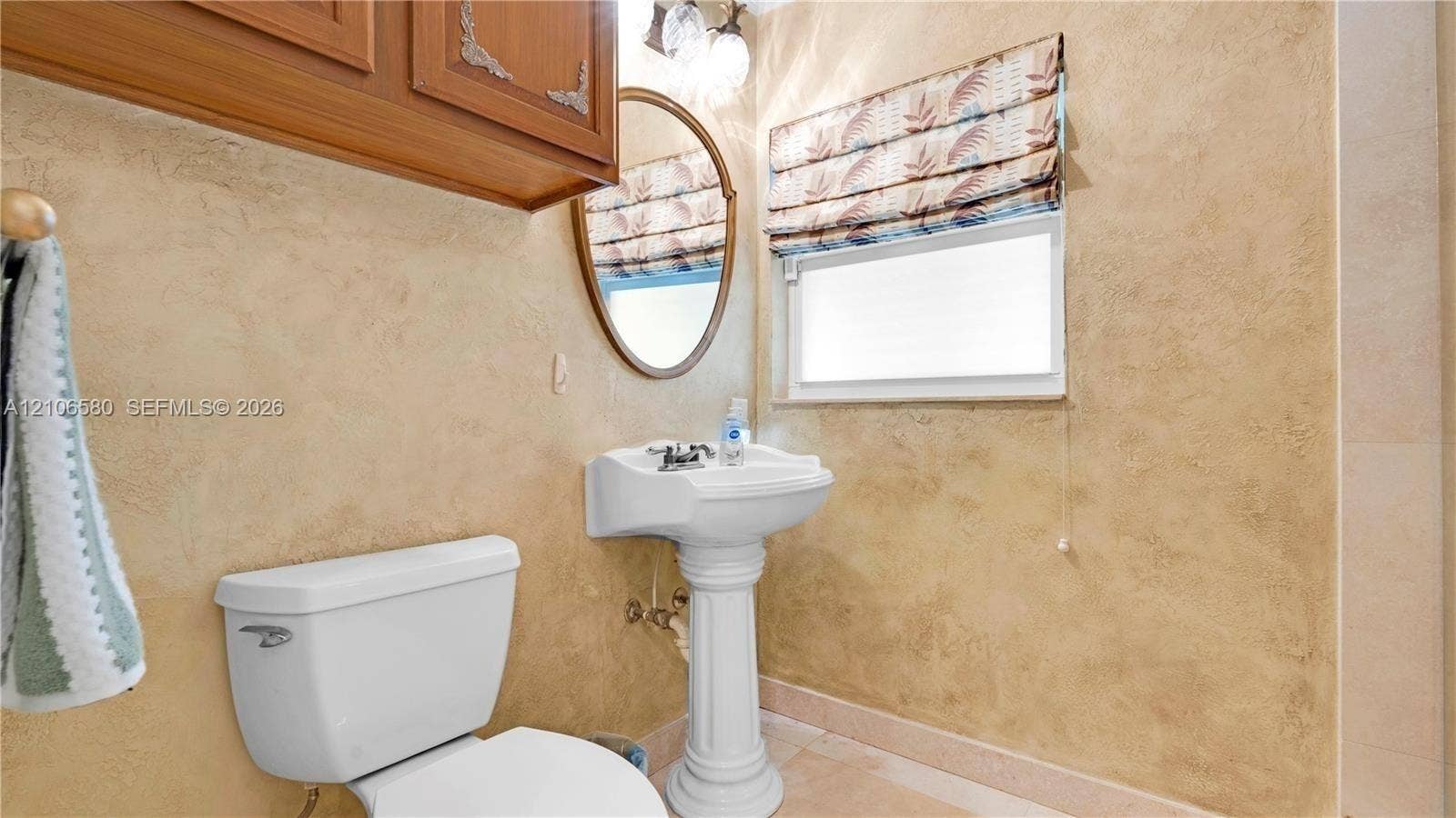 623 NE 17th Way, Fort Lauderdale, Fort Lauderdale, FL 33304 Pedestal sink with chrome faucet, oval mirror, wall-mounted wood-finish cabinetry, and textured wall treatment