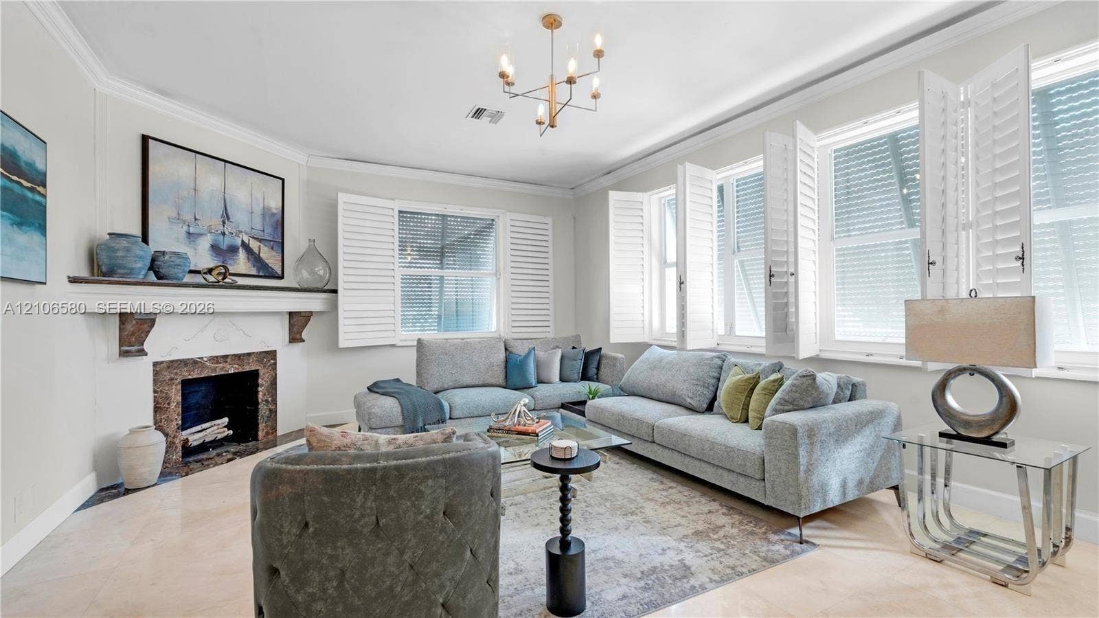 623 NE 17th Way, Fort Lauderdale, Fort Lauderdale, FL 33304 Living room featuring stone fireplace surround with mantel, multi-pane windows with white plantation shutters, crown molding, and polished stone flooring