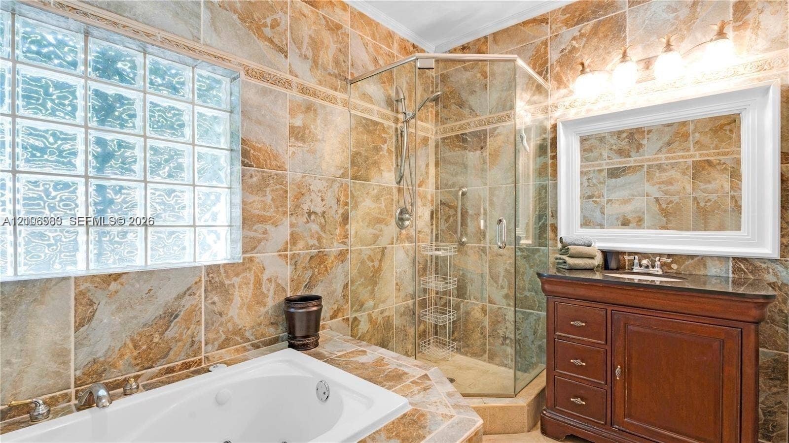 623 NE 17th Way, Fort Lauderdale, Fort Lauderdale, FL 33304 Bathroom featuring full-height stone-finish wall tiling, glass block window, jetted soaking tub, corner glass-enclosed shower, and wood-finish vanity with a thick stone countertop