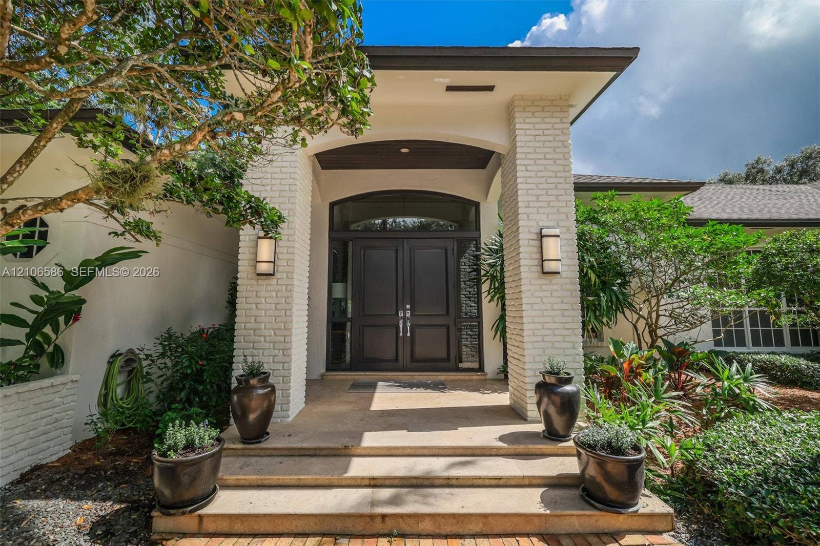 9325 SW 59th Place, Pinecrest, FL 33156 Covered entryway featuring light-colored brick columns, double front doors with arched transom windows, and stone steps