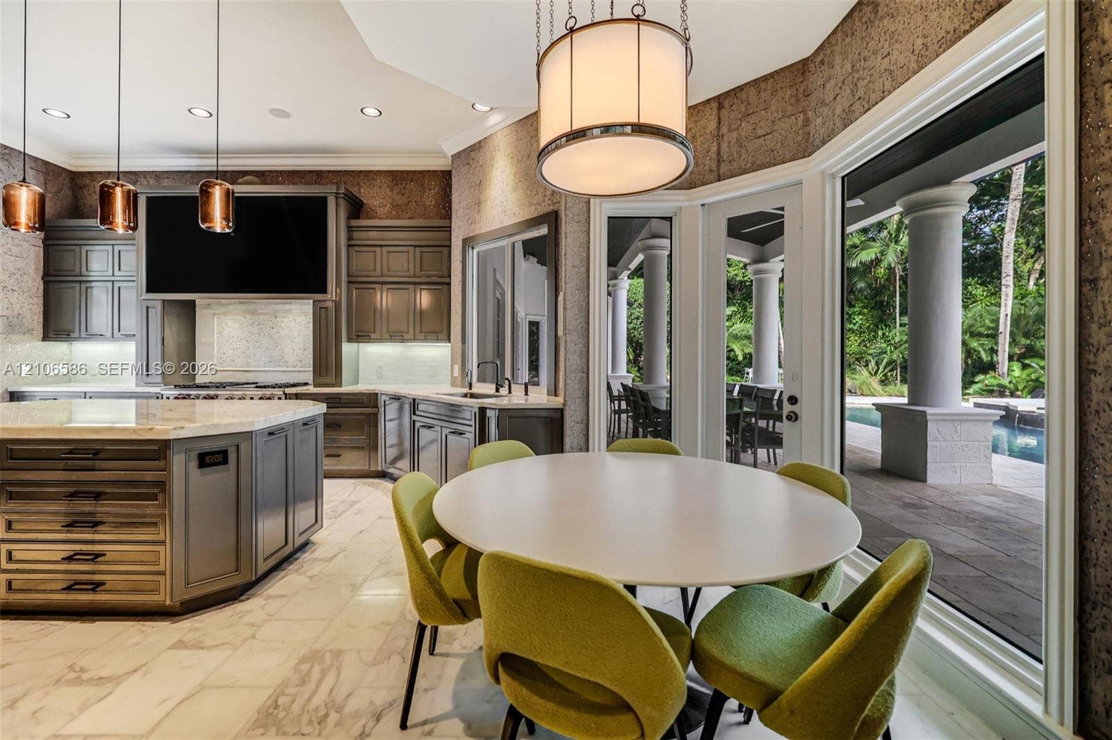 9325 SW 59th Place, Pinecrest, FL 33156 Kitchen featuring custom cabinetry, an oversized central island with stone countertop, large-format tile flooring, textured wall finishes, and expansive glass doors opening to a columned patio
