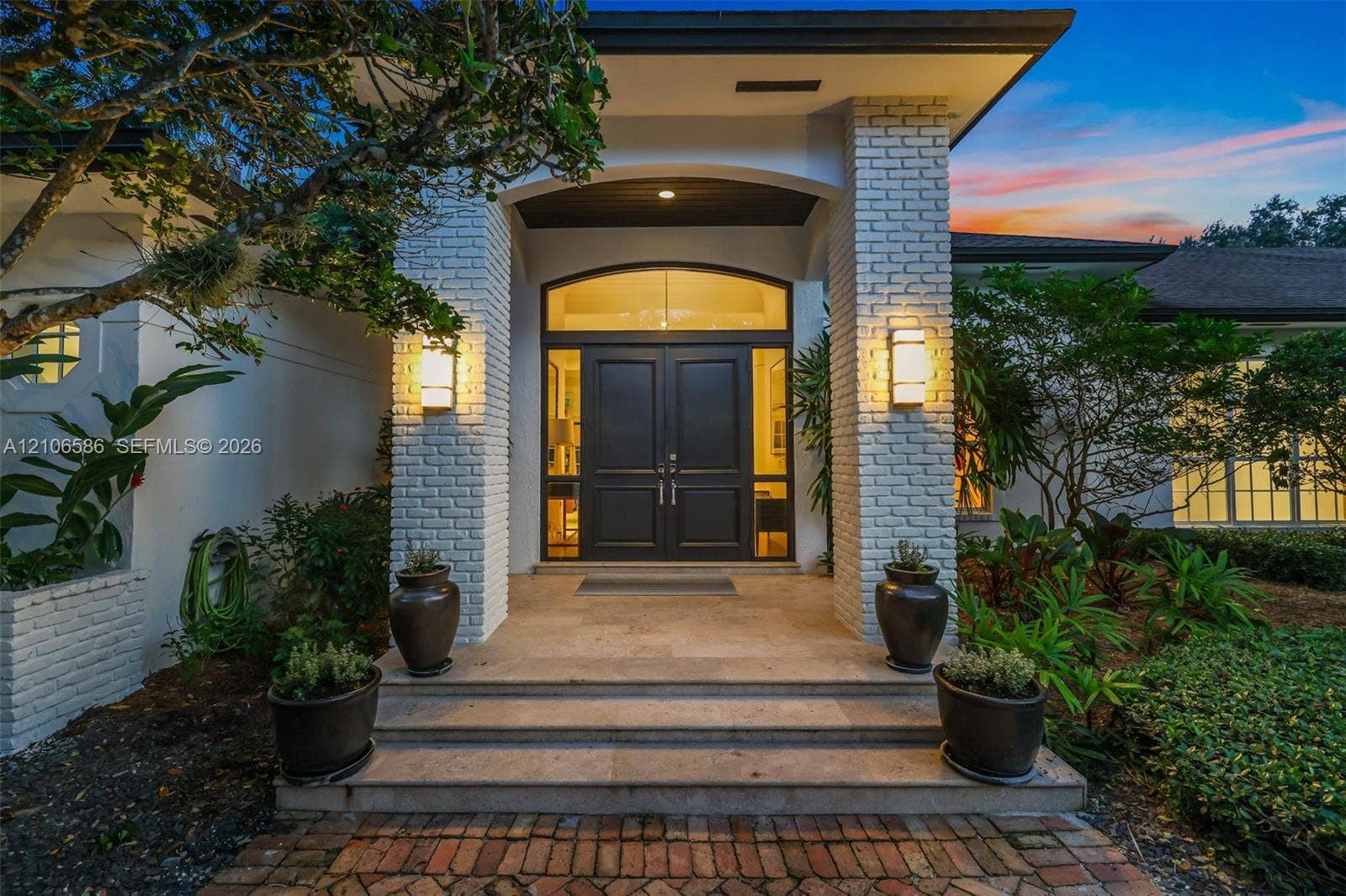 9325 SW 59th Place, Pinecrest, FL 33156 Exterior entrance featuring painted brick pillars, double front doors with an arched glass transom, stone step entry, and wall-mounted light fixtures