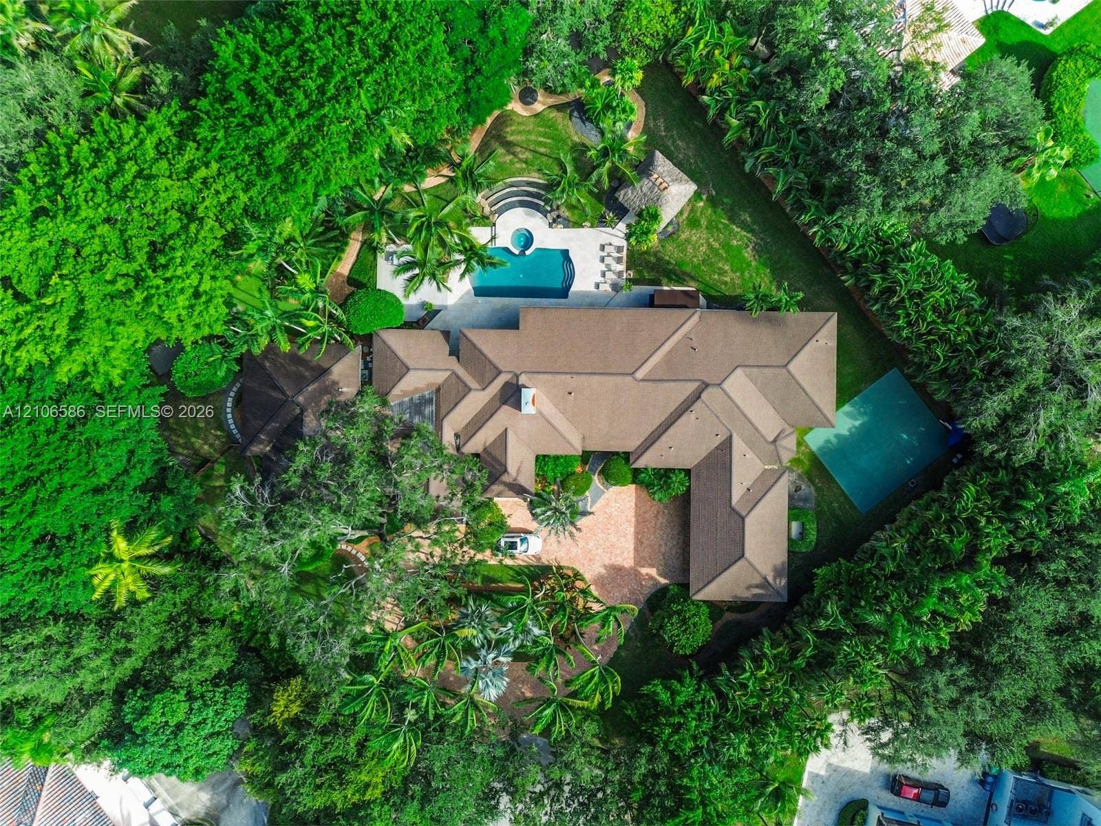 9325 SW 59th Place, Pinecrest, FL 33156 Aerial perspective of a sprawling property featuring a paved circular driveway, a swimming pool with spa, a tennis court, and mature perimeter landscaping