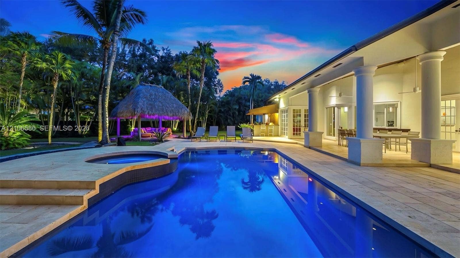 9325 SW 59th Place, Pinecrest, FL 33156 Custom swimming pool with integrated spa, expansive stone patio, covered lanai featuring structural columns, and a thatched-roof cabana