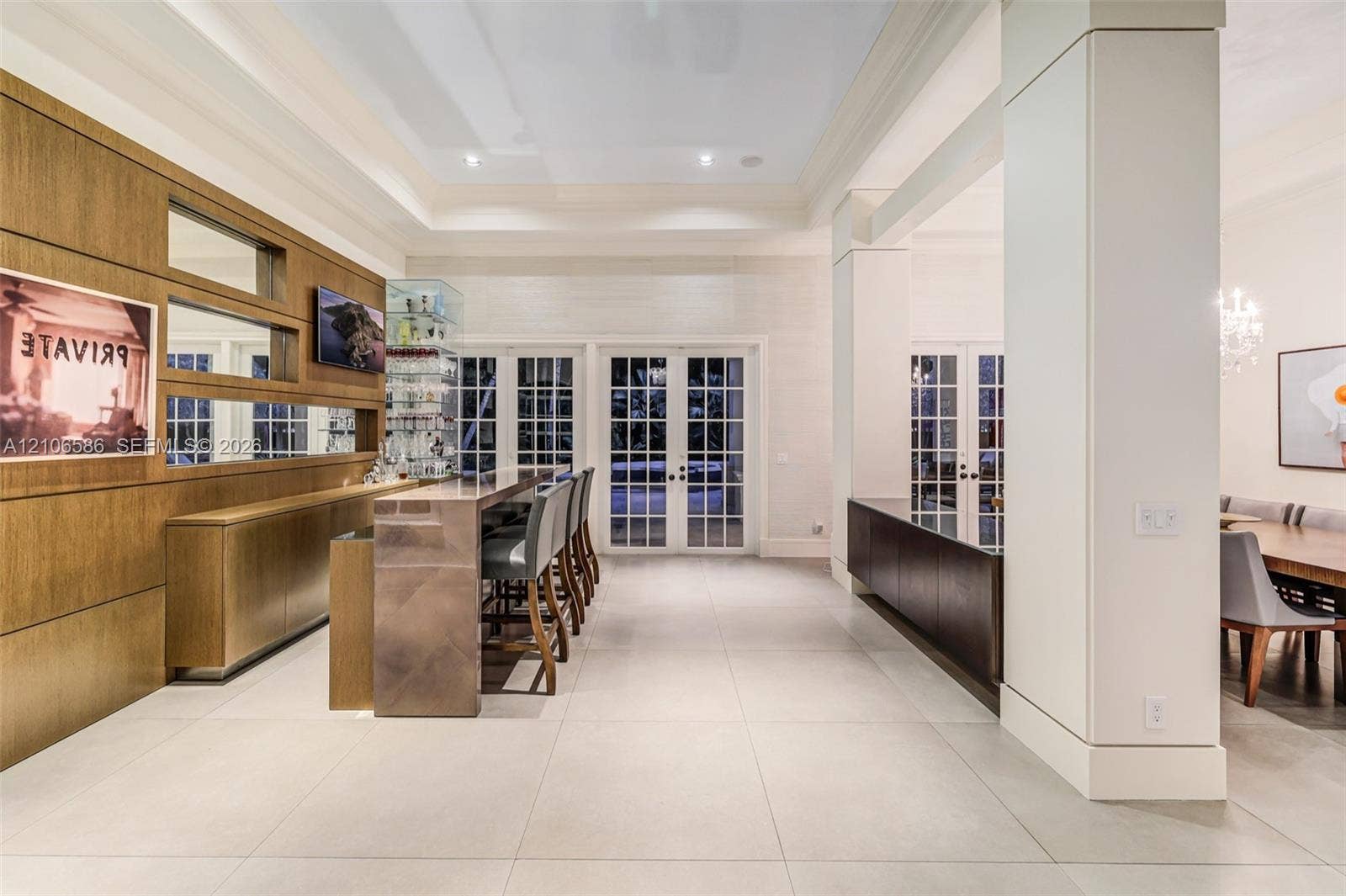 9325 SW 59th Place, Pinecrest, FL 33156 Custom bar w/ wood-paneled wall, lighted niches, glass display cabinet & bar seating, French doors to the terrace & formal dining beyond