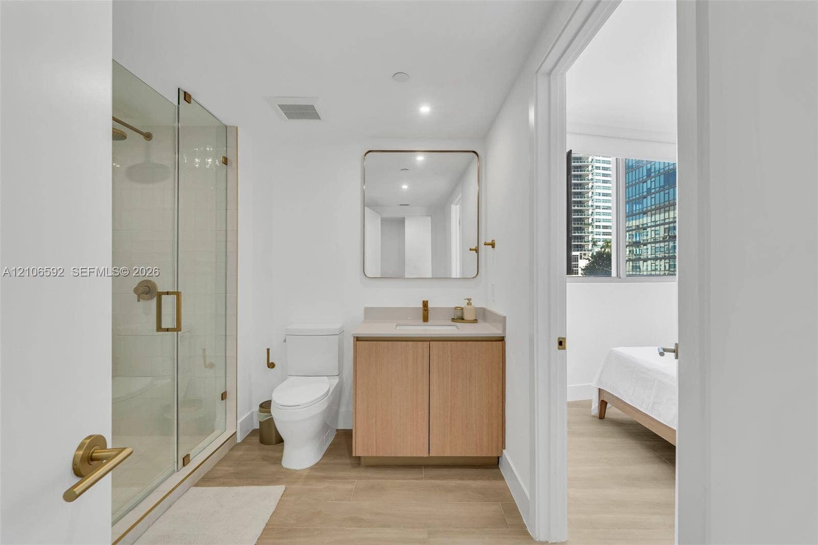 90 NE 32, #612, Miami, Miami, FL 33127 Bathroom featuring a glass-enclosed shower, light wood-finish cabinetry with a stone countertop, wall-mounted rectangular mirror with rounded corners, and metallic fixtures