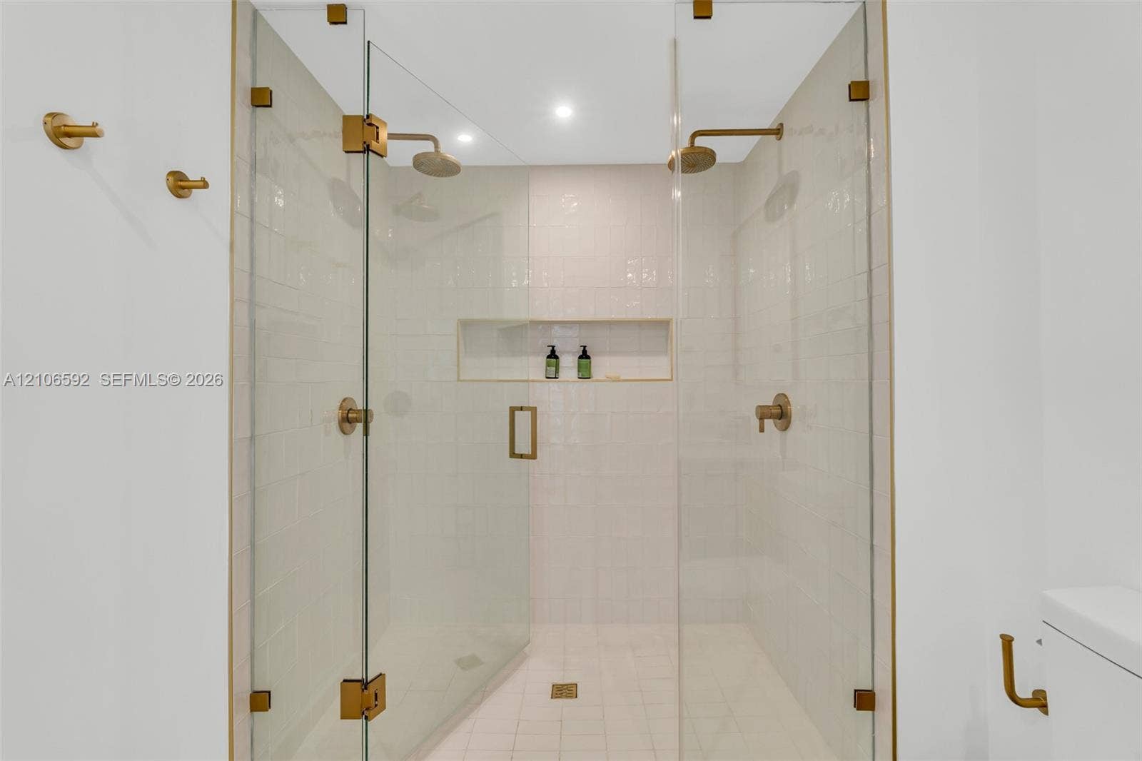 90 NE 32, #612, Miami, Miami, FL 33127 Walk-in shower featuring a frameless glass enclosure, gold-tone hardware, dual rainfall showerheads, integrated wall niche, and white subway tile wall surrounds