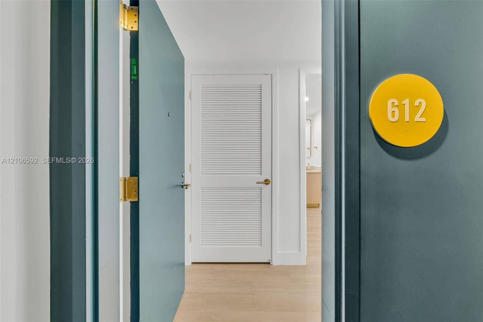 90 NE 32, #612, Miami, Miami, FL 33127 Entryway featuring a solid door with a circular yellow room identification plaque, brass hinges, white louvered door, and wood-finish flooring