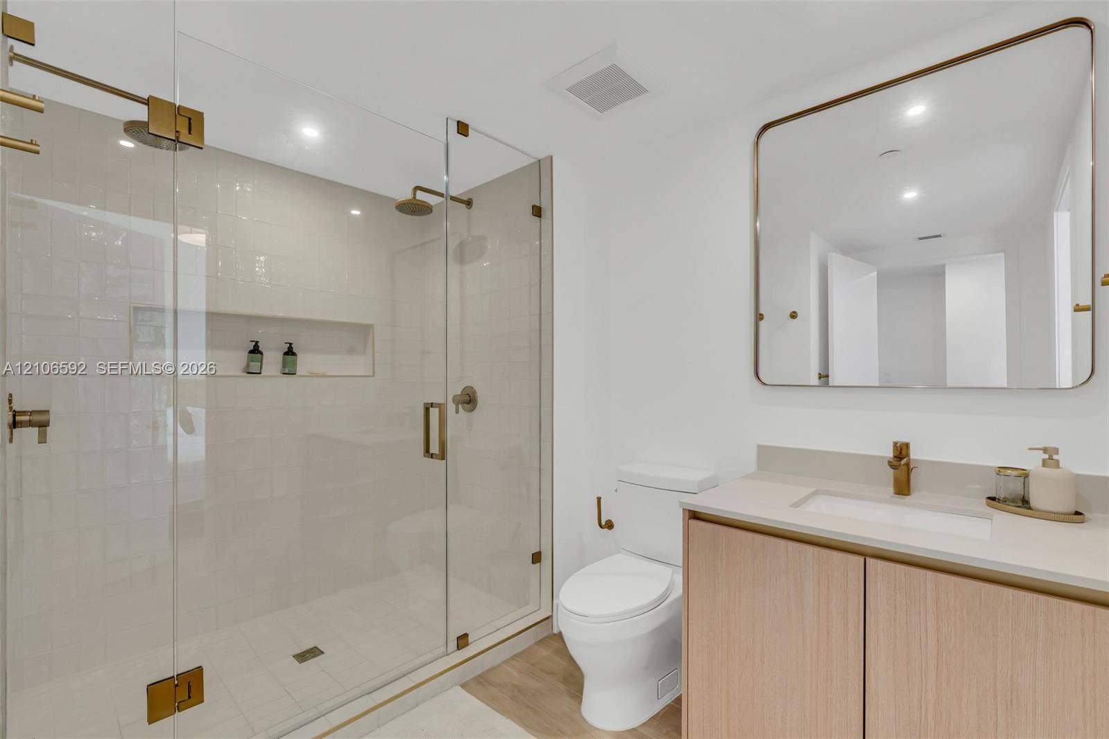 90 NE 32, #612, Miami, Miami, FL 33127 Frameless glass walk-in shower with integrated tile niche, wood-finish vanity cabinet, solid surface countertop, brass-tone hardware, and rounded-corner wall mirror
