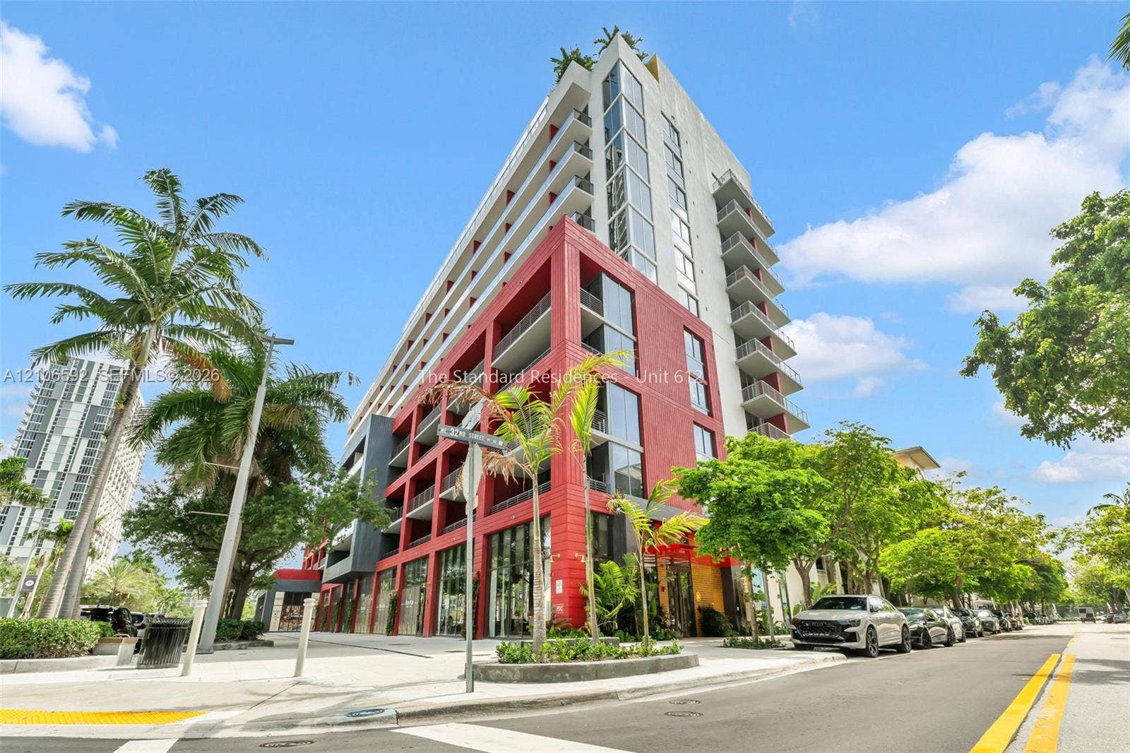 90 NE 32, #612, Miami, Miami, FL 33127 Mid-rise residential building featuring a vibrant red masonry facade, full-height glass curtain walls, private balconies, and ground-level storefronts
