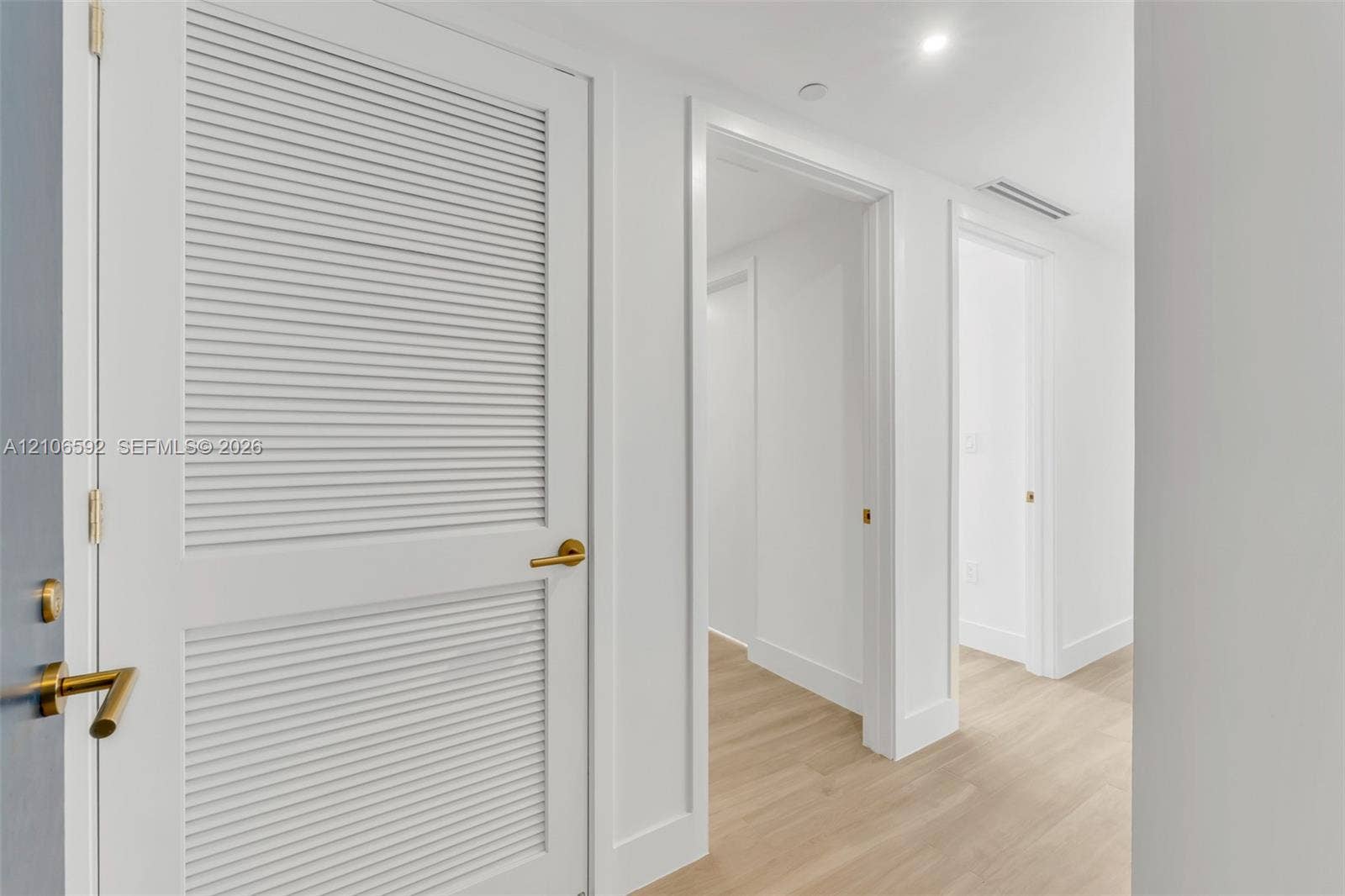 90 NE 32, #612, Miami, Miami, FL 33127 Interior hallway featuring wood-finish flooring, bright white walls, and white louvered doors with satin brass hardware