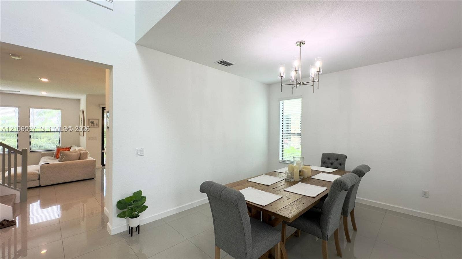 Open-concept dining area featuring high ceilings, neutral tile flooring, and a multi-arm chandelier
