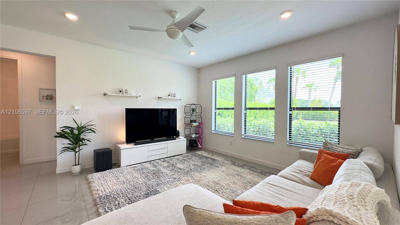 Living area featuring neutral tile flooring, recessed lighting, a modern ceiling fan, and three windows with horizontal blinds