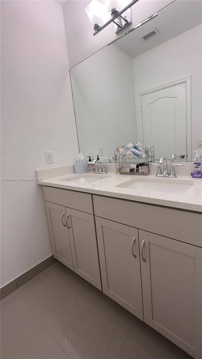 Upstairs guest bathroom Dual-sink vanity featuring light-toned cabinetry, light-toned stone-finish countertop, undermount sinks, and a large-format frameless mirror with mounted lighting fixture