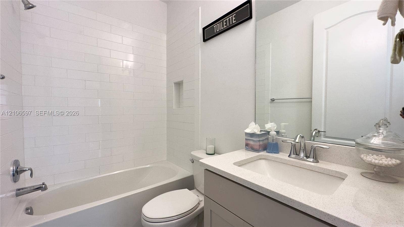 First floor guest Bathroom featuring a white subway tile shower surround, integrated wall niche, quartz countertop, and vanity cabinet with an undermount sink