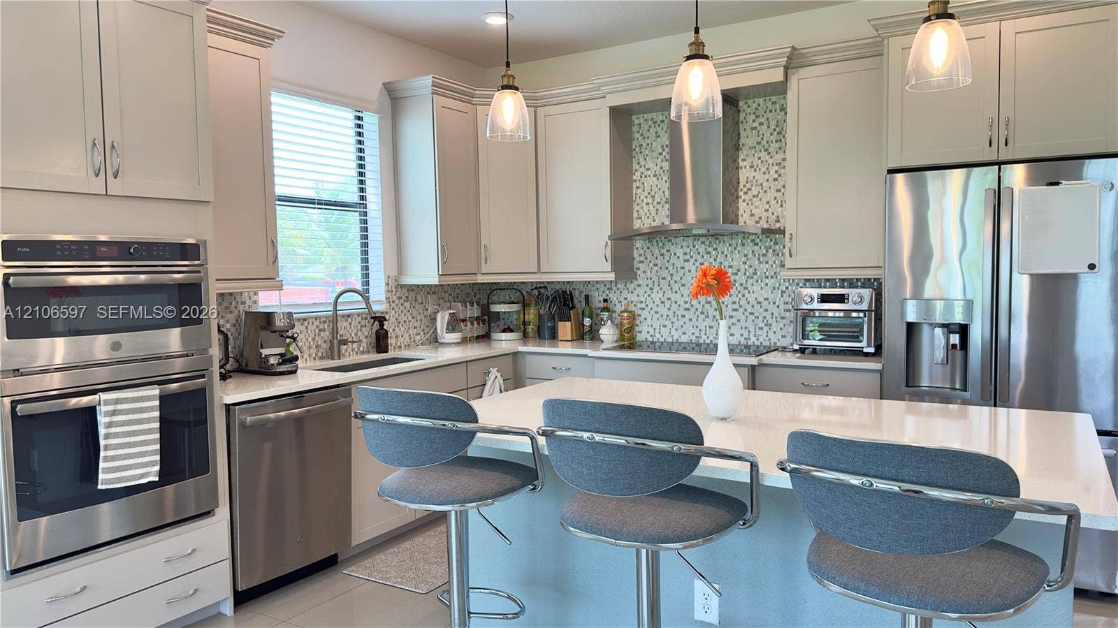 Kitchen featuring light-toned shaker cabinetry, stone-surface countertops, a mosaic tile backsplash, stainless steel built-in double ovens, and a central island with pendant lighting