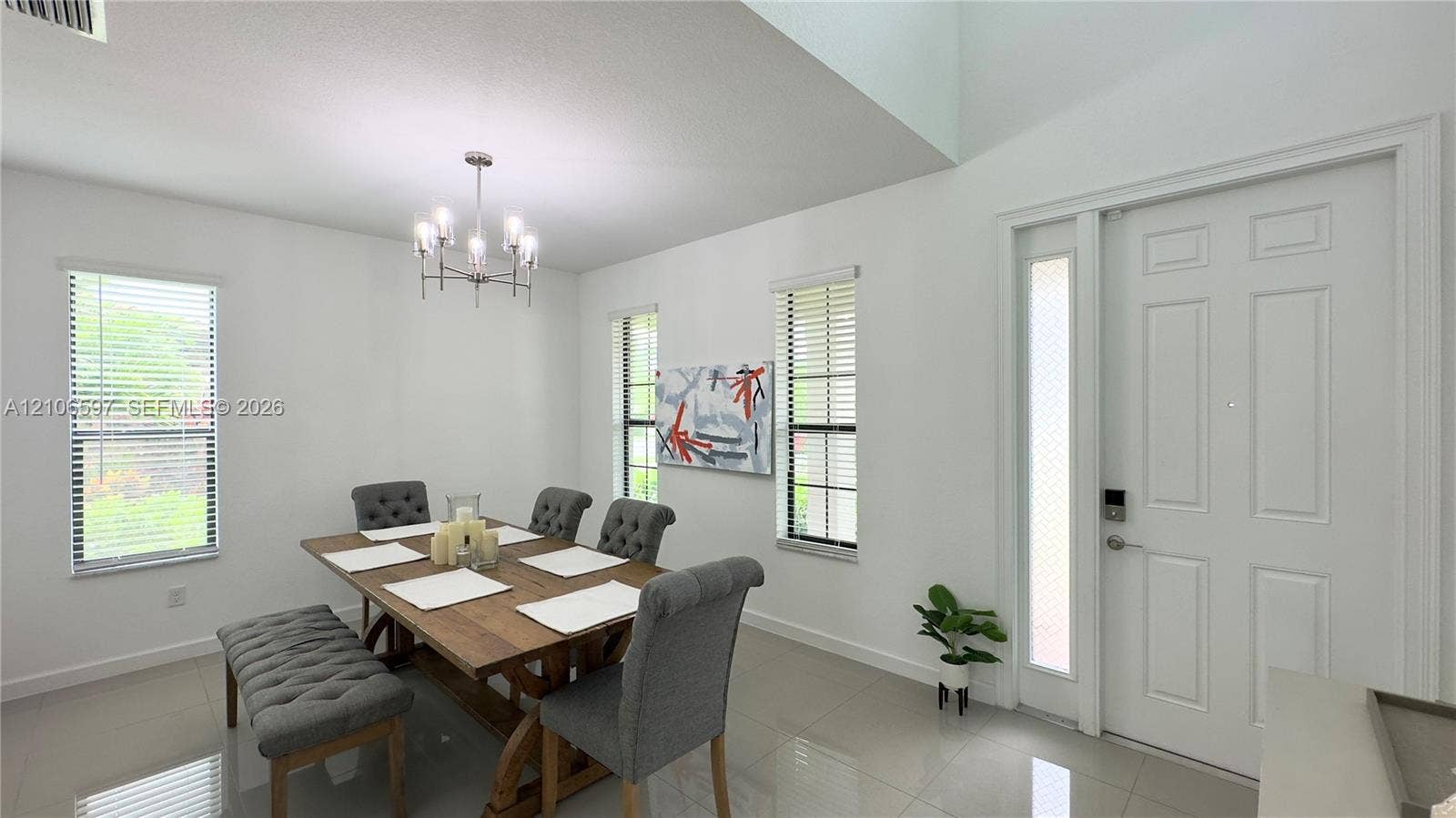 High-ceiling entryway featuring neutral tile flooring, multi-paneled door with integrated glass sidelight, and a decorative multi-arm chandelier