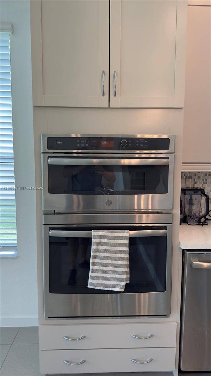Built-in stainless steel double wall oven and microwave combination unit integrated into cabinetry with light-toned flat-panel upper cupboards and lower storage drawers