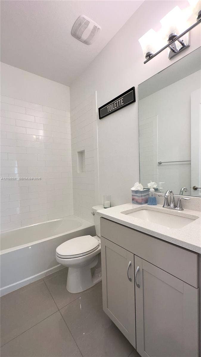 First floor guest Bathroom featuring a white subway tile shower surround with an integrated recessed niche, light gray cabinetry, a neutral stone-finish countertop, and polished chrome fixtures