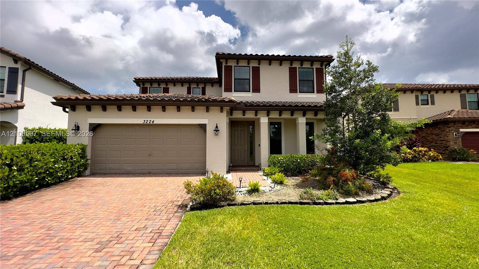 Two-story exterior featuring a stucco faade, decorative corbel roof supports, a multi-textured clay tile roof, and a paved brick driveway and walkway