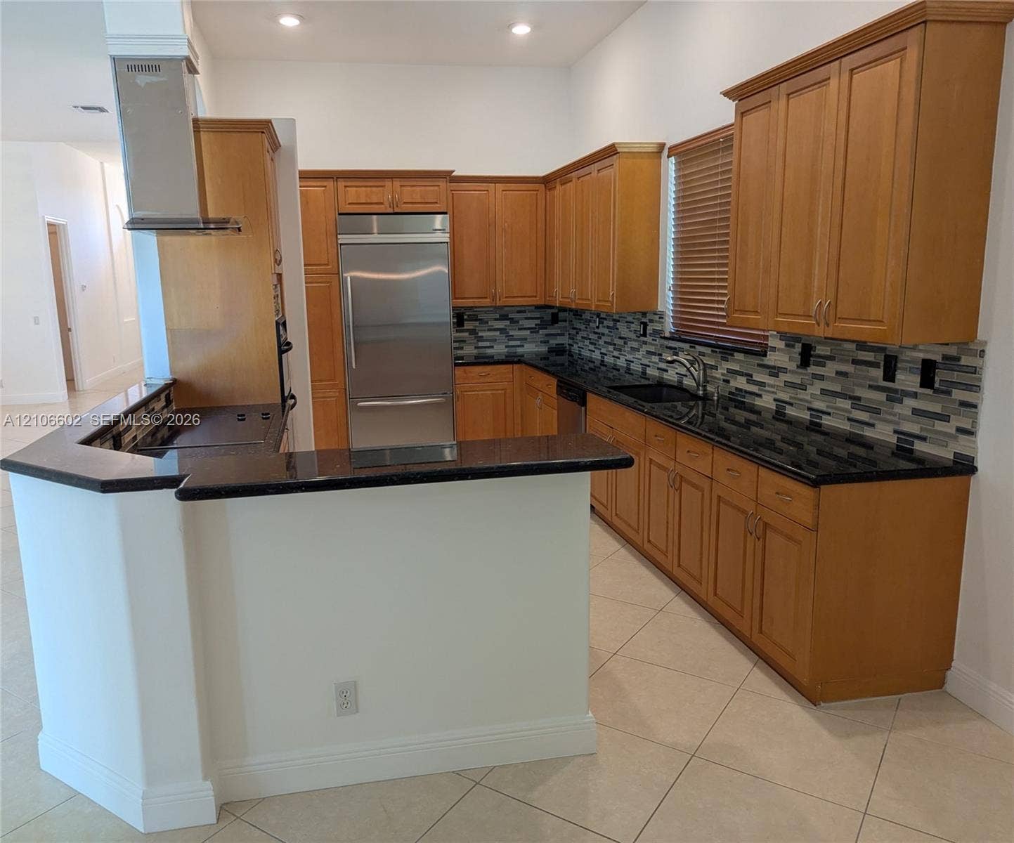 15274 Fiorenza Circle, Delray Beach, FL 33446 Kitchen featuring wood cabinetry, dark stone countertops, stainless steel refrigerator, tile backsplash, and a stainless steel wall-mounted range hood