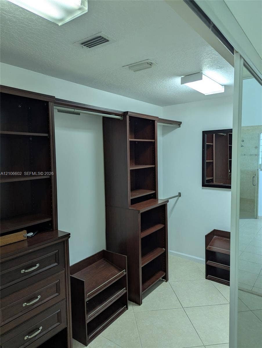 15274 Fiorenza Circle, Delray Beach, FL 33446 Walk-in closet featuring dark wood-finish built-in cabinetry, integrated shelving units, multi-tier hanging rods, and light-tone tile flooring