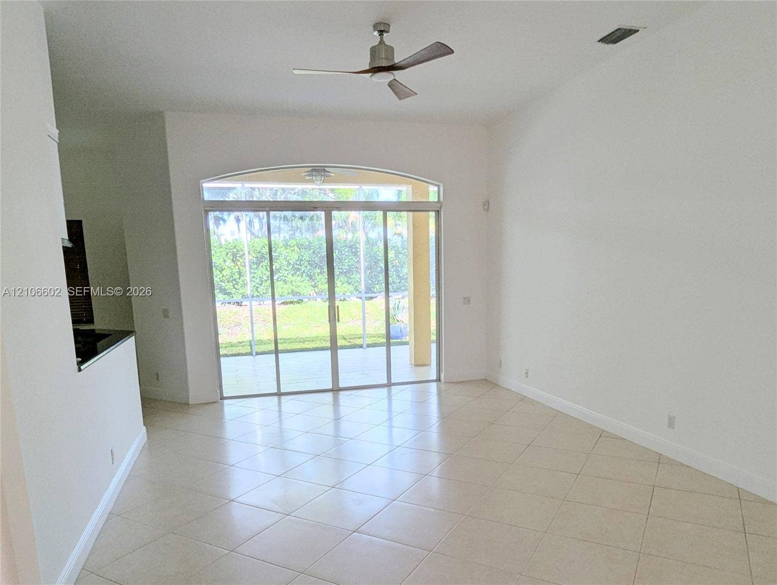 15274 Fiorenza Circle, Delray Beach, FL 33446 Interior space featuring vaulted ceilings, neutral tile flooring, a multi-blade ceiling fan, and arched sliding glass doors opening to a screened-in lanai