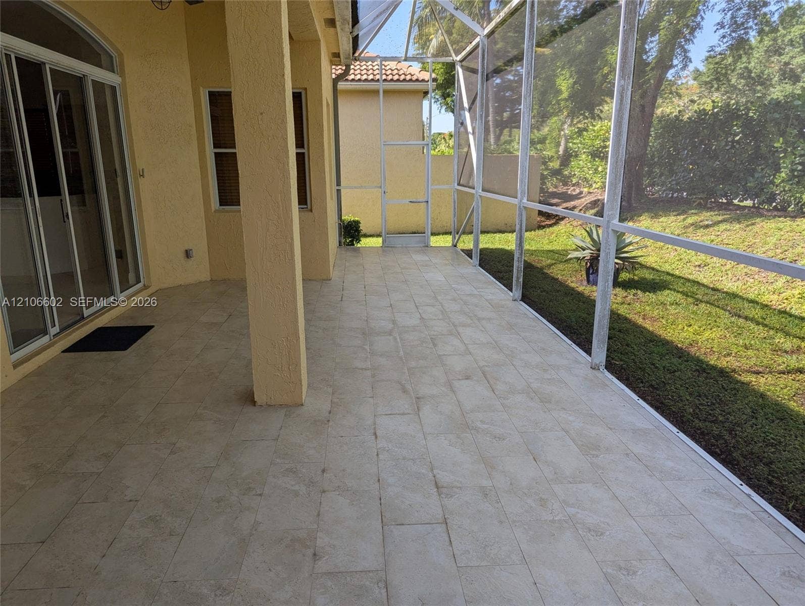 15274 Fiorenza Circle, Delray Beach, FL 33446 Covered patio featuring stone-tile flooring, a screened-in enclosure, sliding glass door access, and a manicured exterior lawn