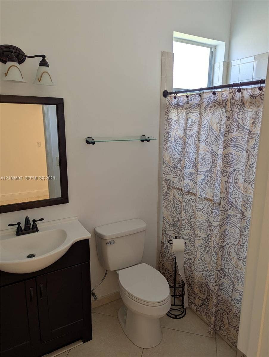 15274 Fiorenza Circle, Delray Beach, FL 33446 Bathroom featuring a dark-finish vanity with a white integrated basin, dual-handle faucet, framed wall mirror, two-light fixture, and ceramic tile flooring