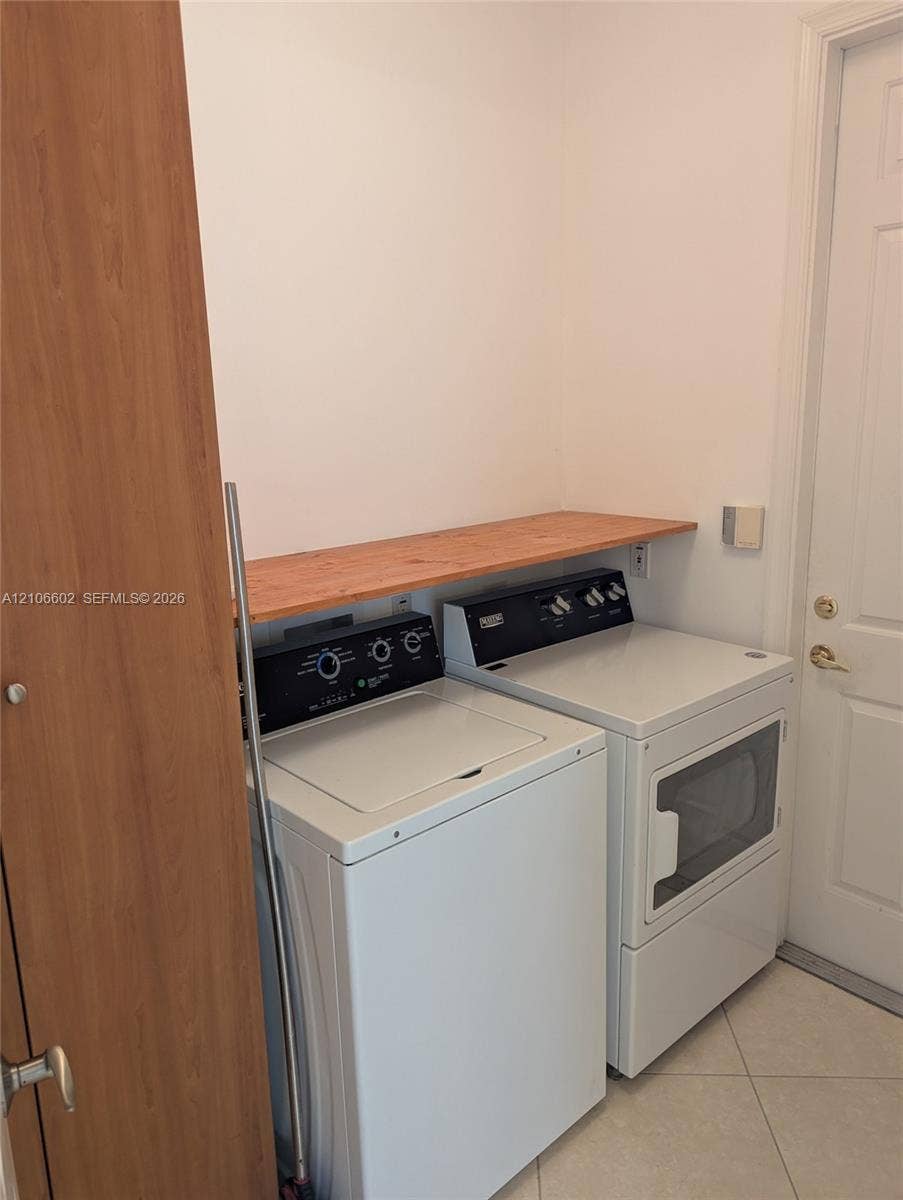 15274 Fiorenza Circle, Delray Beach, FL 33446 Utility area featuring ceramic tile flooring, a natural wood-finish storage shelf, and a multi-panel door with gold-tone hardware