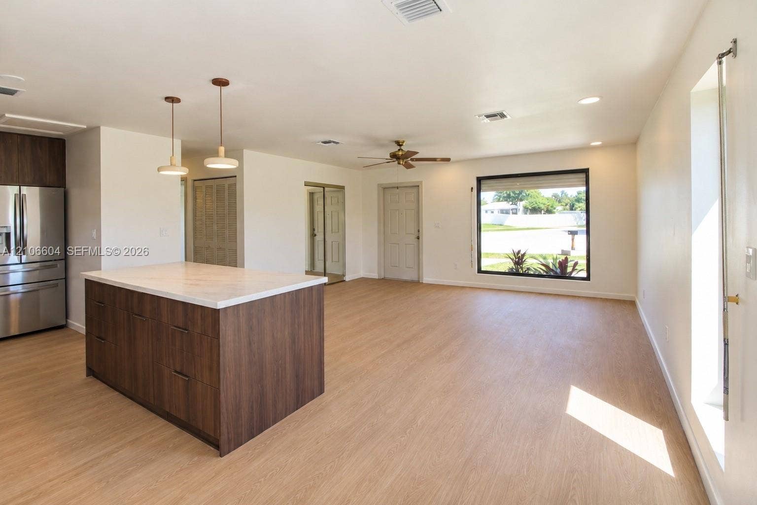 Open-concept space featuring wood-finish flooring, a kitchen island with stone-finish countertop, stainless steel refrigerator, and dual pendant lighting