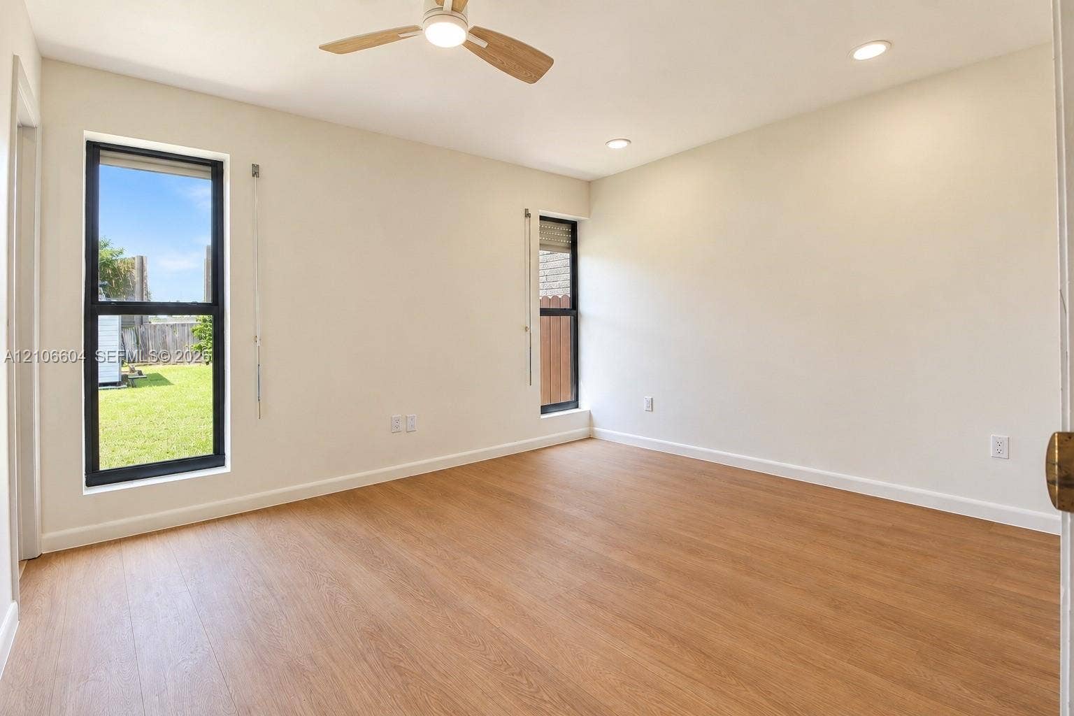 Neutral-toned interior featuring wood-finish flooring, recessed lighting, a ceiling fan with light fixture, and large windows with black frames