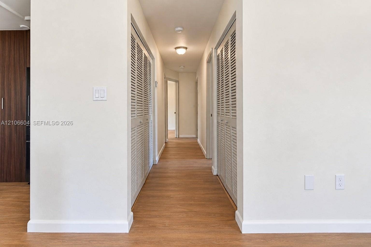 Hallway featuring wood-finish flooring, dual louvered-door closets, and flush-mount ceiling lighting