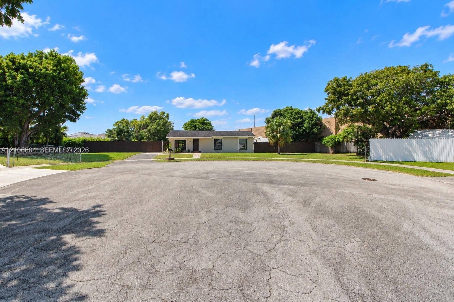 Single-story residence featuring a low-slope roof, expansive front lawn, mature trees, and perimeter fencing